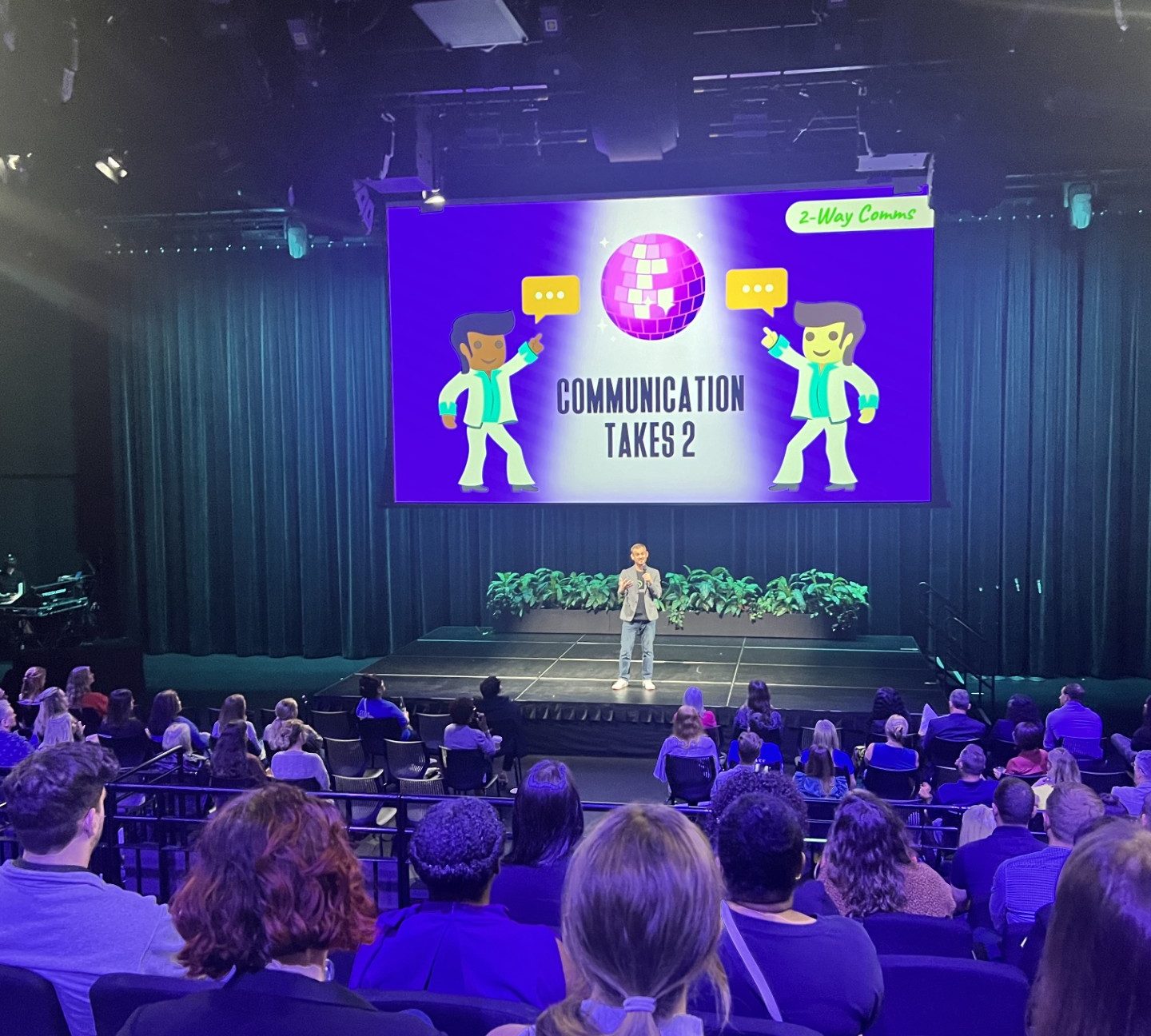 Luke Goetting speaking on a large stage to a packed audience